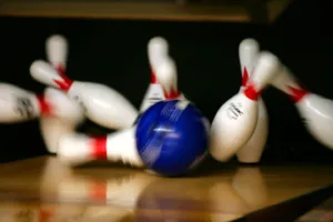 A blue bowling ball is crashing into bowling pins.