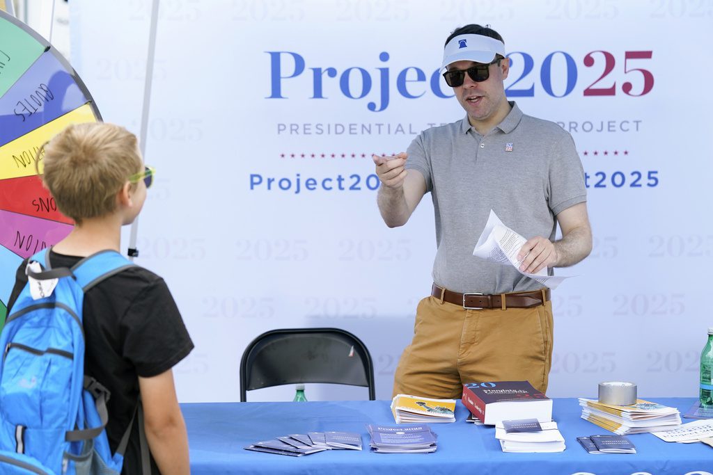 Spencer Chretien, right, talks to a young fairgoer at the Project 2025 tent at the Iowa State Fair, Aug. 14, 2023, in Des Moines, Iowa. With more than a year to go before the 2024 election, a constellation of conservative organizations is preparing for a possible second White House term for Donald Trump. The Project 2025 effort is being led by the Heritage Foundation think tank. (AP Photo/Charlie Neibergall)