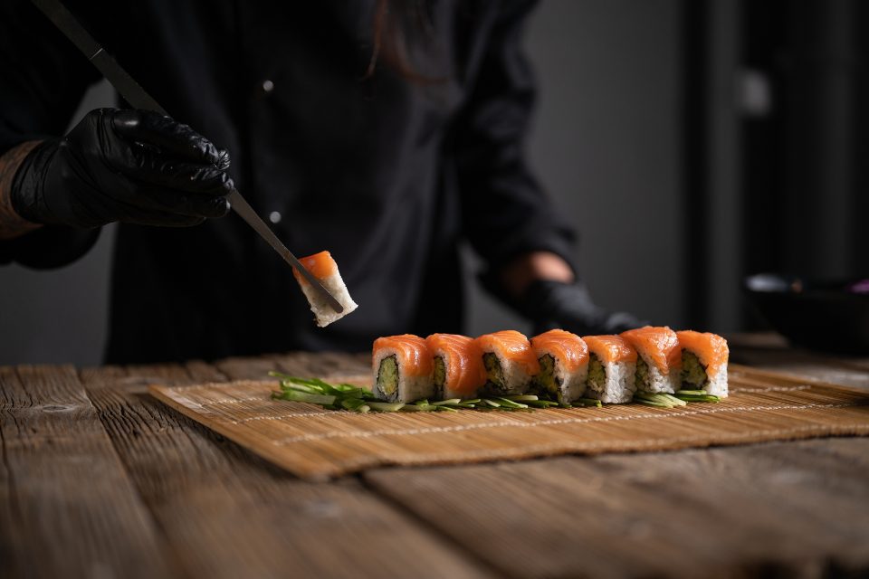 A person dressed in black eats sushi with chopsticks.