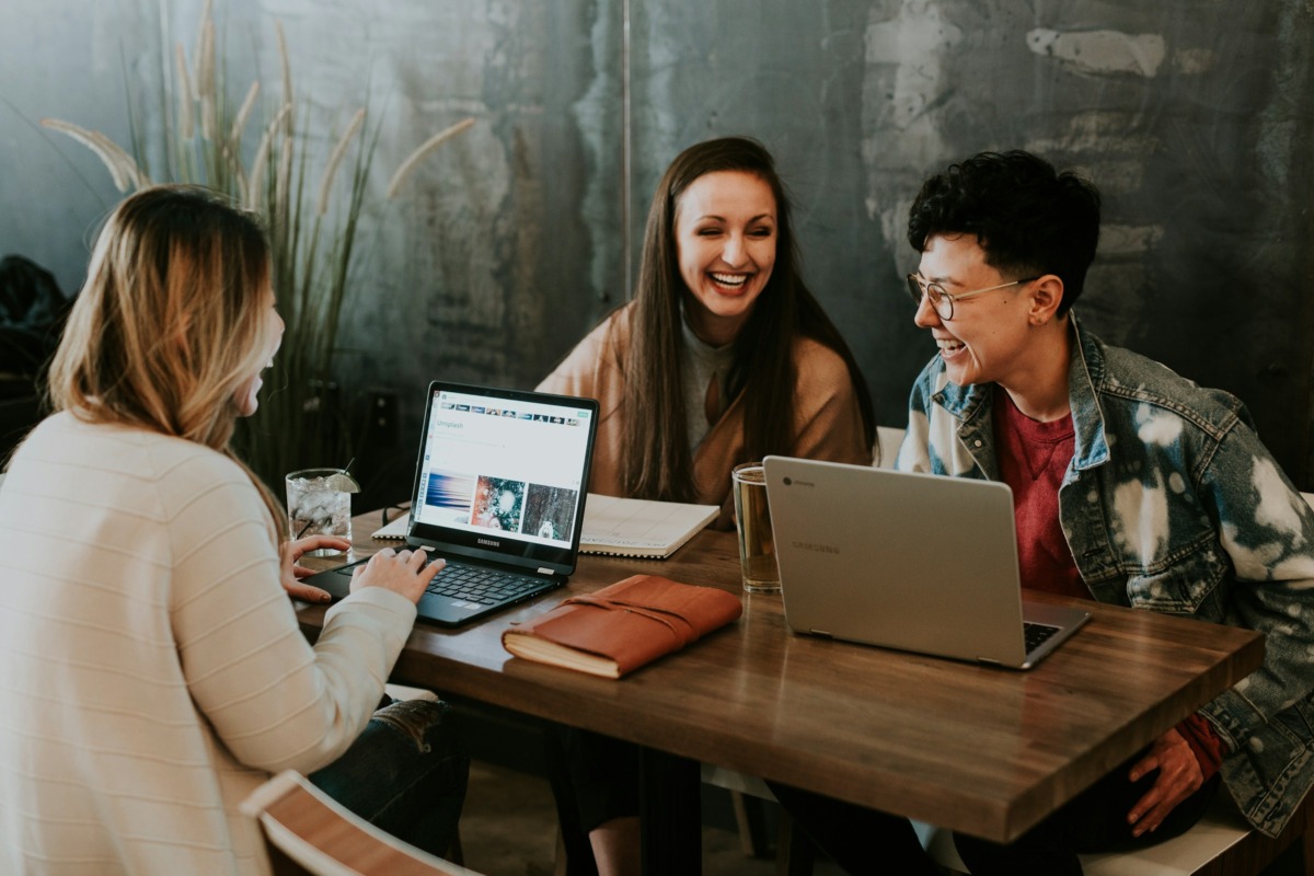 Group of friends laughing at a table with open laptops.