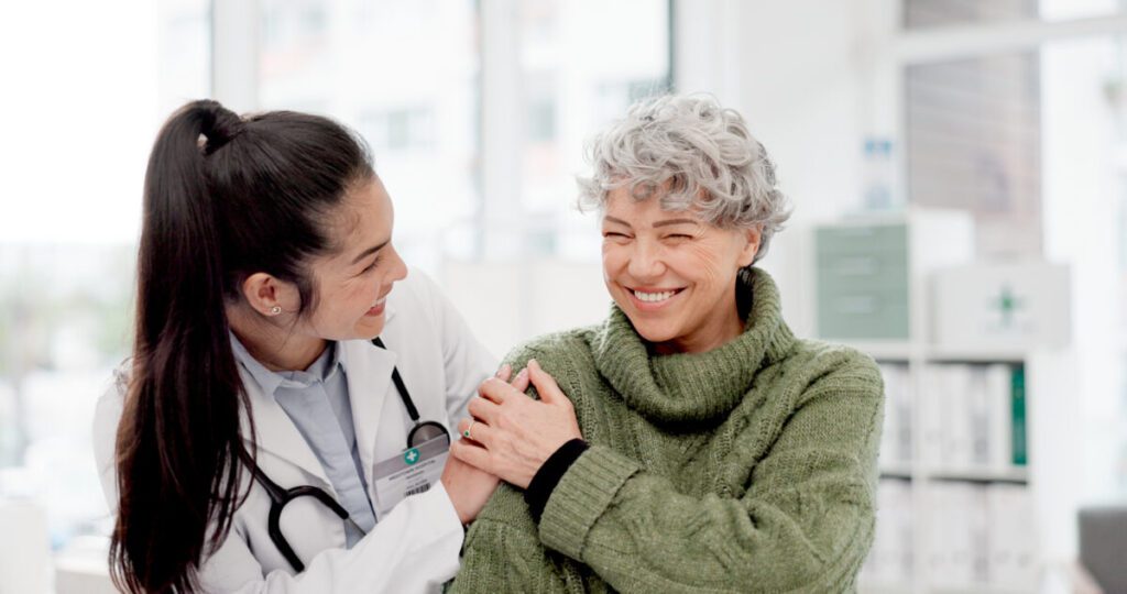 Happy, care and face of a doctor with a woman for medical trust, healthcare and help. Laughing, hug and portrait of a young nurse with a senior patient and love during a consultation at a clinic.