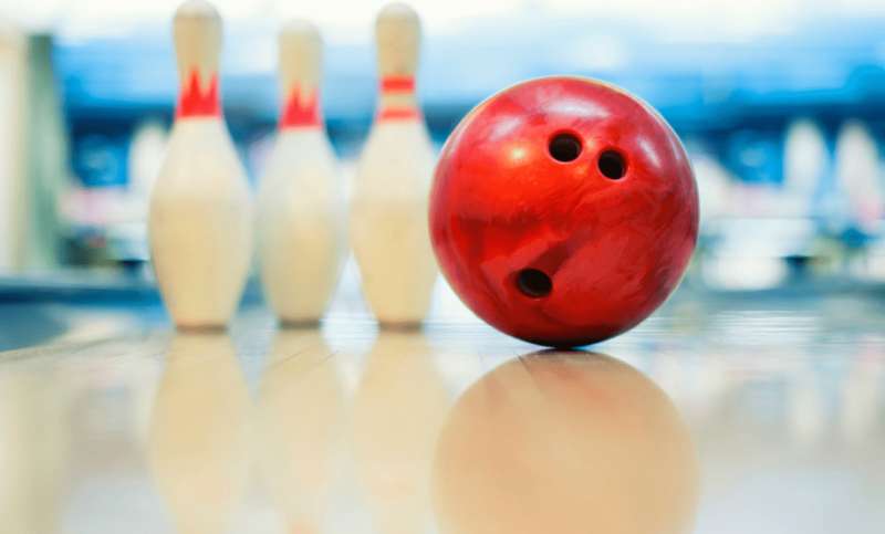 A red bowling ball and three bowling pins sitting on a clean bowling alley.