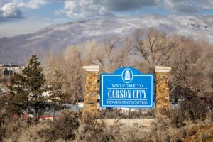 A highway welcome sign for Carson City with a serene winter scene.