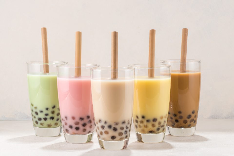 Five colorful boba tea drinks with wooden straws.