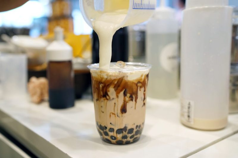 Milk is being poured into a cup of boba tea.