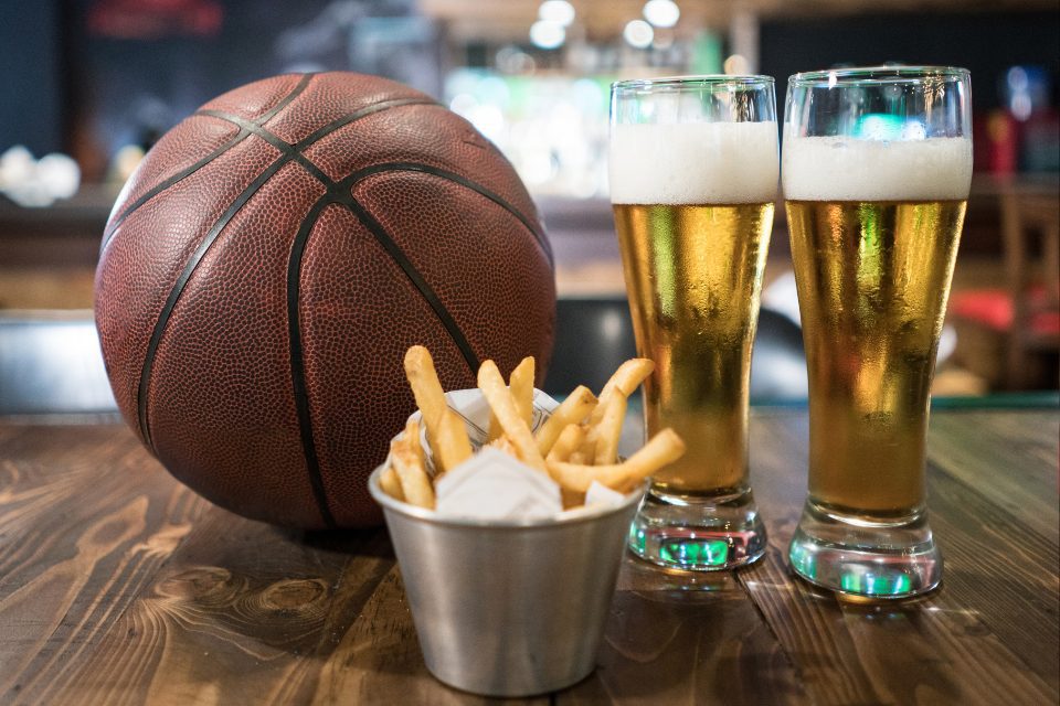 A basketball, two beers, and a side of fries on a table at a sports bar.