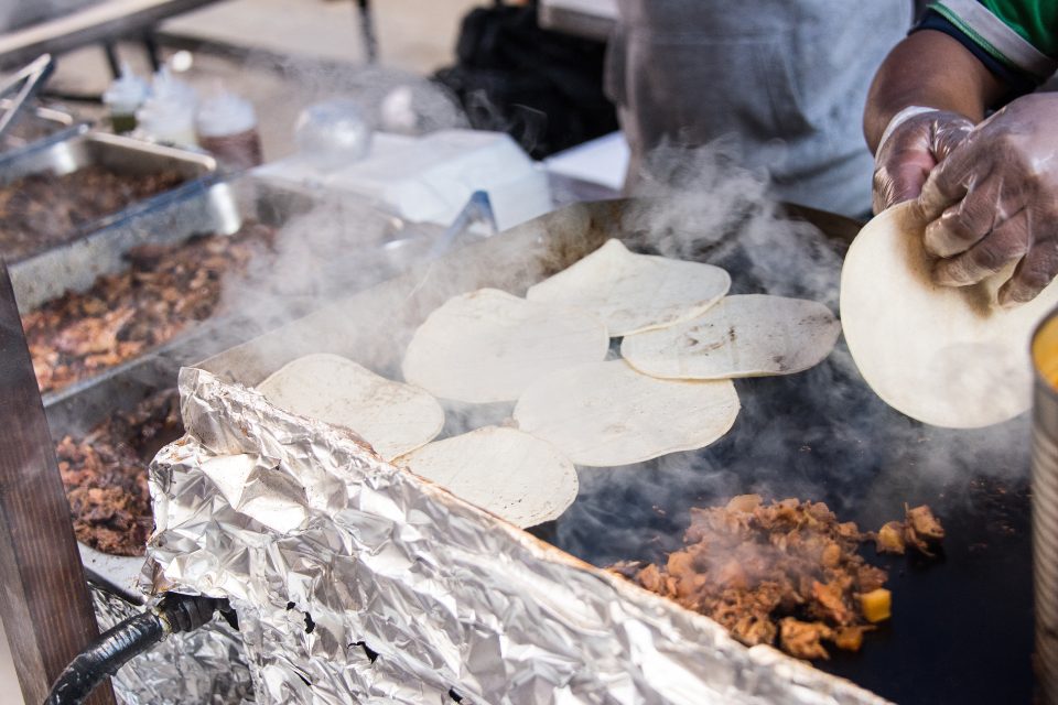 A street vendor cooking tacos on a flat top grill.