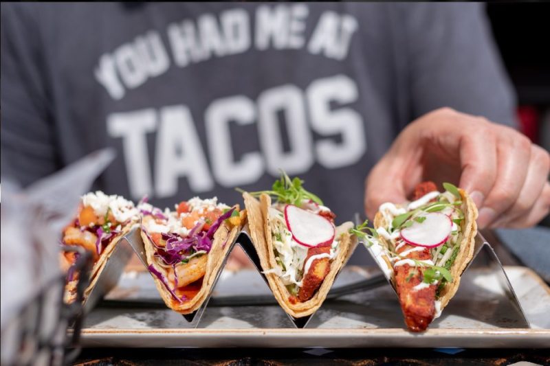 A man wearing a shirt that says, "you had me at tacos" eating tacos.