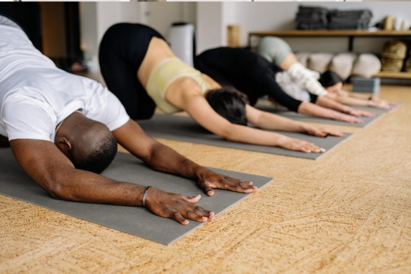 Four men and women relax into a downward dog post on gray yoga mats.