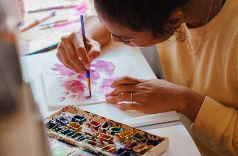 Young female artist with her head down, painting with a paint brush.