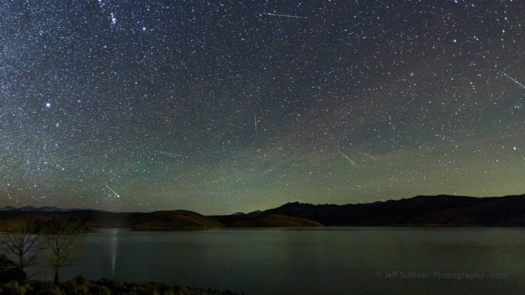 Night sky with stars and a mountain in the background near a lake.