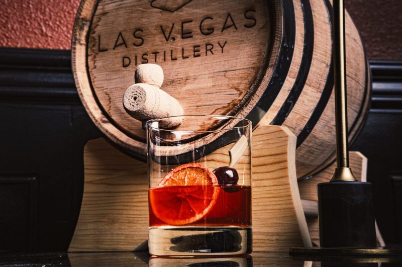 a wooden barrel reading "las vegas distillery" with a glass of alcohol in front of it