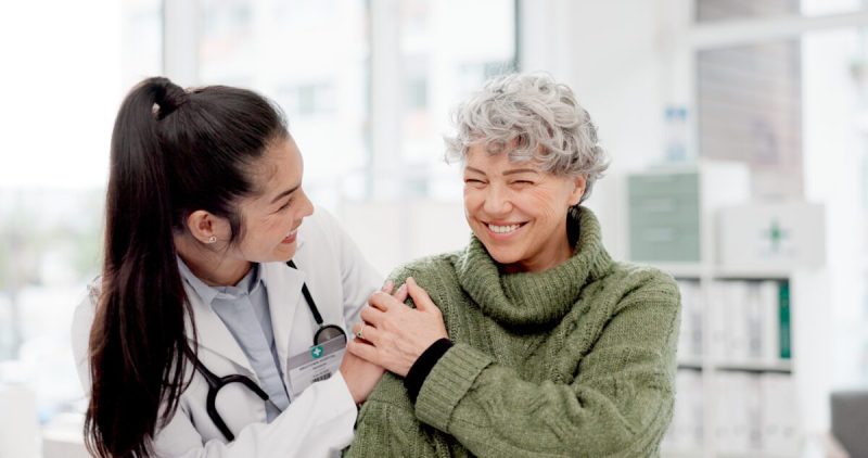 Happy, care and face of a doctor with a woman for medical trust, healthcare and help. Laughing, hug and portrait of a young nurse with a senior patient and love during a consultation at a clinic.