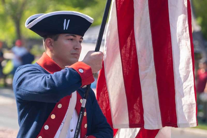 A man in historic uniform carries an American flag in a parade