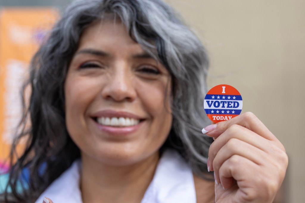A Hispanic woman holding a "I Voted Today" sticker after voting.